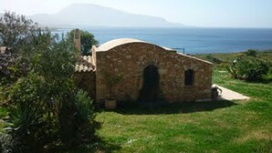 Un edificio de piedra con una pequeña entrada arqueada, rodeado de vegetación y con vistas a un cuerpo de agua.