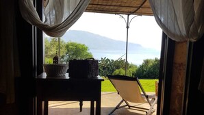 Una habitación con una cama, una mesa con una cesta y un farol, y vistas a un césped y montañas a través de una puerta abierta.