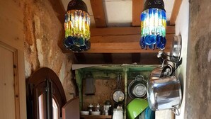 Una cocina rústica con vigas de madera, un estante verde con utensilios de cocina, una tetera y una ventana con cortinas.