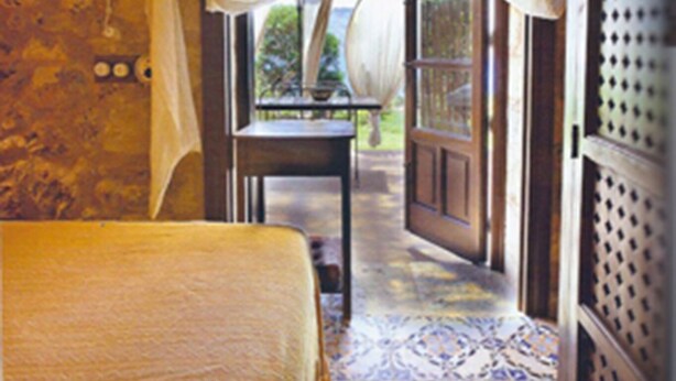 Una habitación con cama, una mesa y vistas a través de una puerta abierta.