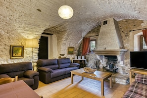 A rustic living room with stone walls, a fireplace, a sofa, a coffee table, and a television.