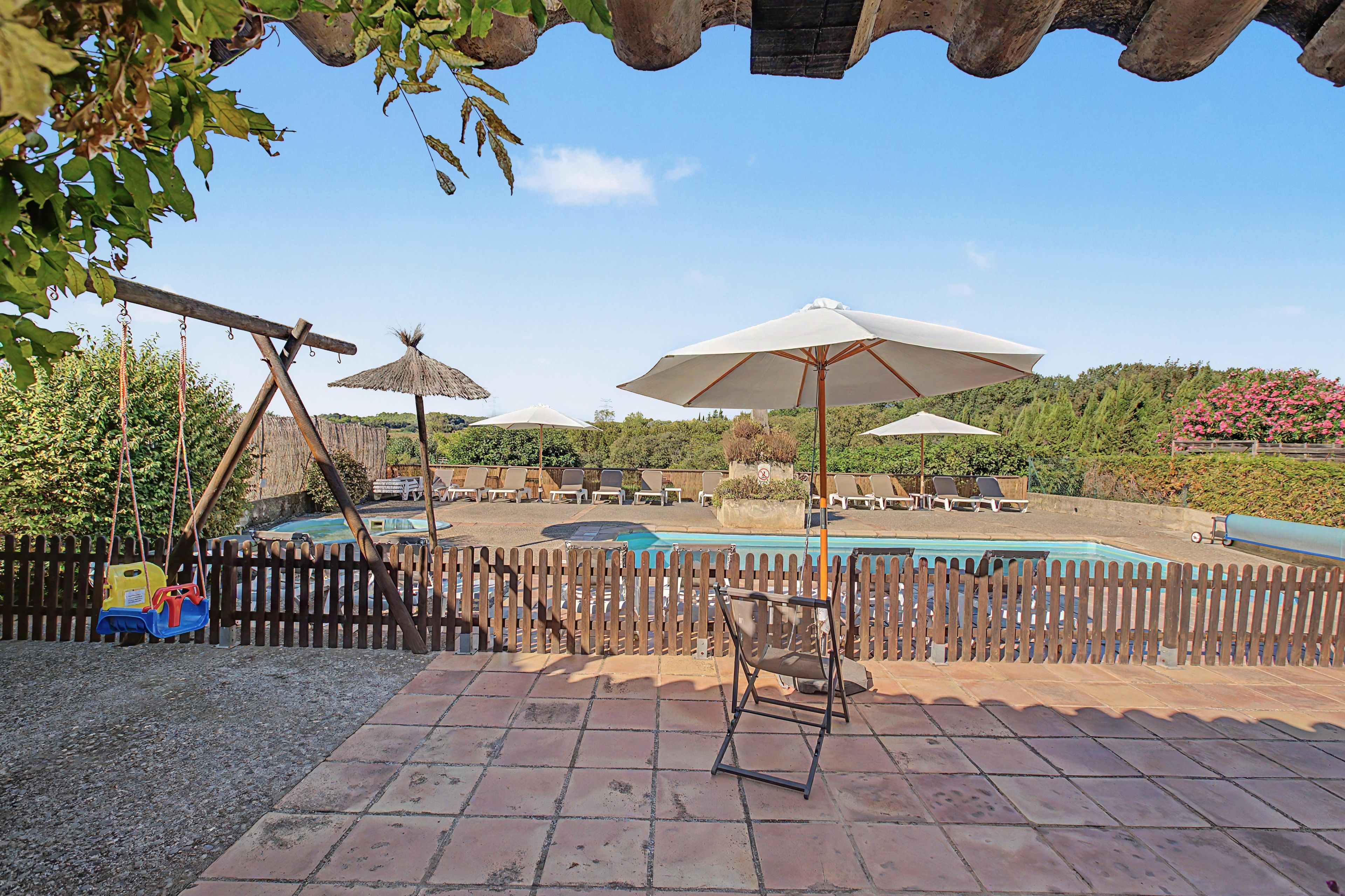 A pool area with a wooden fence, lounge chairs, and umbrellas.