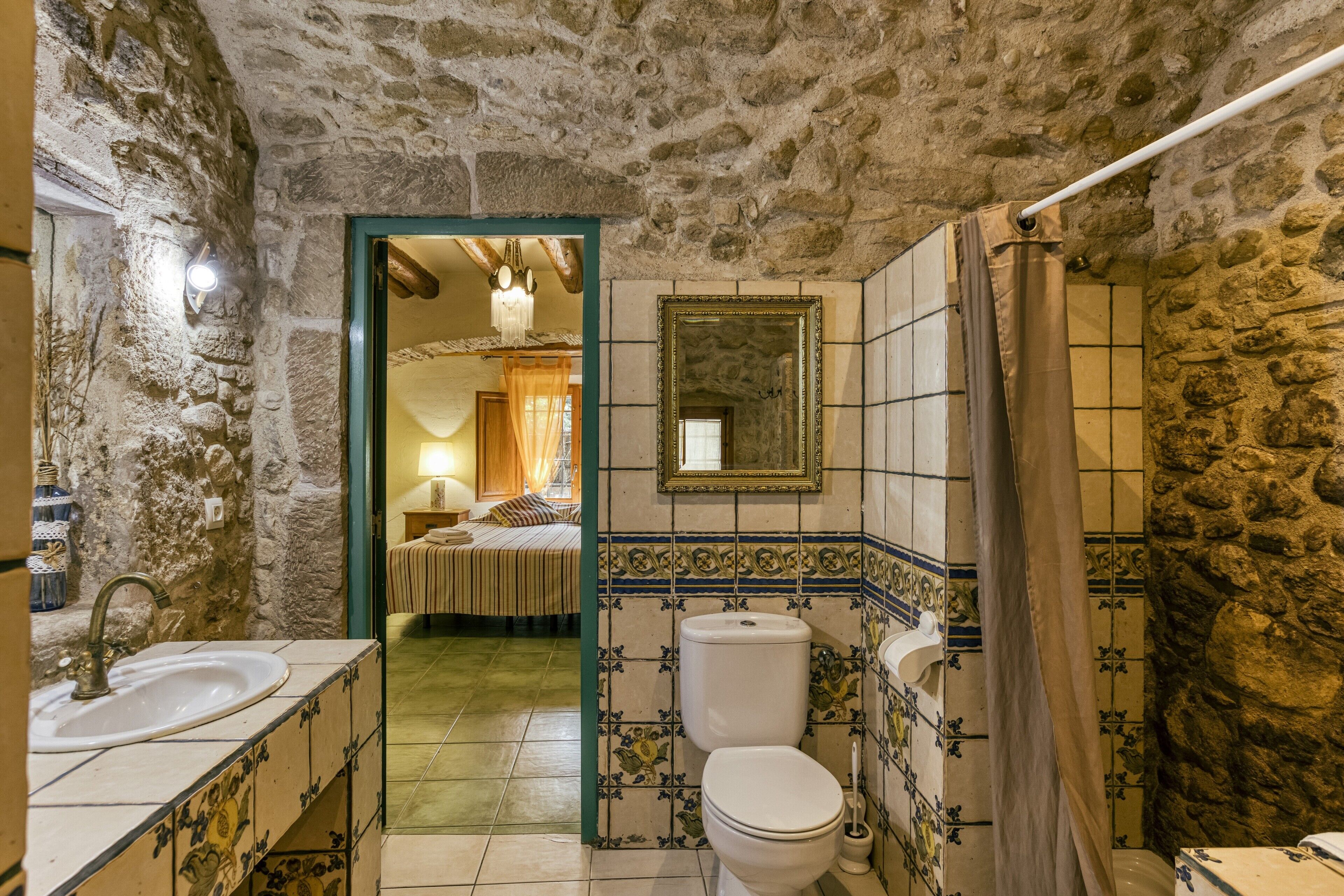 A bathroom with a stone wall, a sink, a toilet, and a mirror.