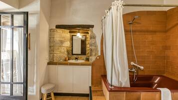 Un baño con pared de piedra, una bañera de madera, un lavamanos con espejo y una ducha con cortina.