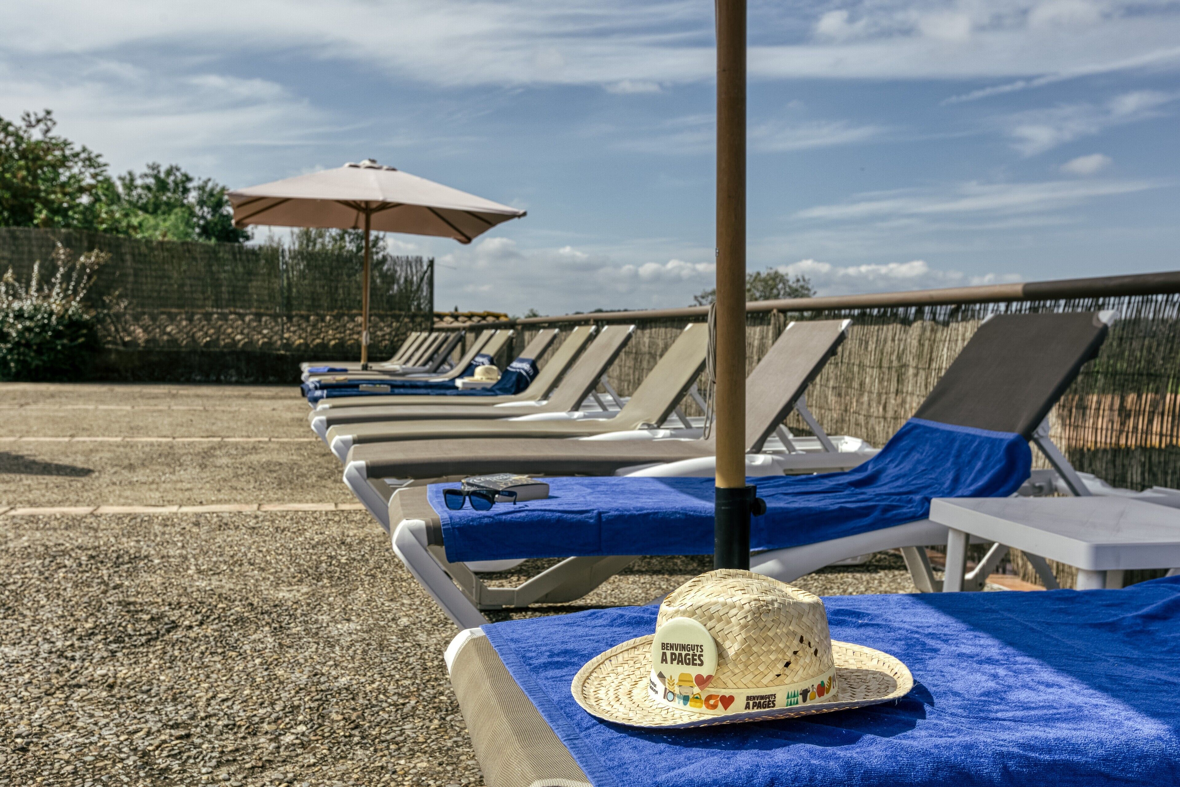 Una fila de sillas de playa con toallas azules y un sombrero de paja.