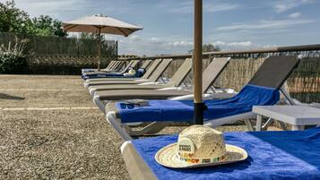 Una fila de sillas de playa con toallas azules y un sombrero de paja.