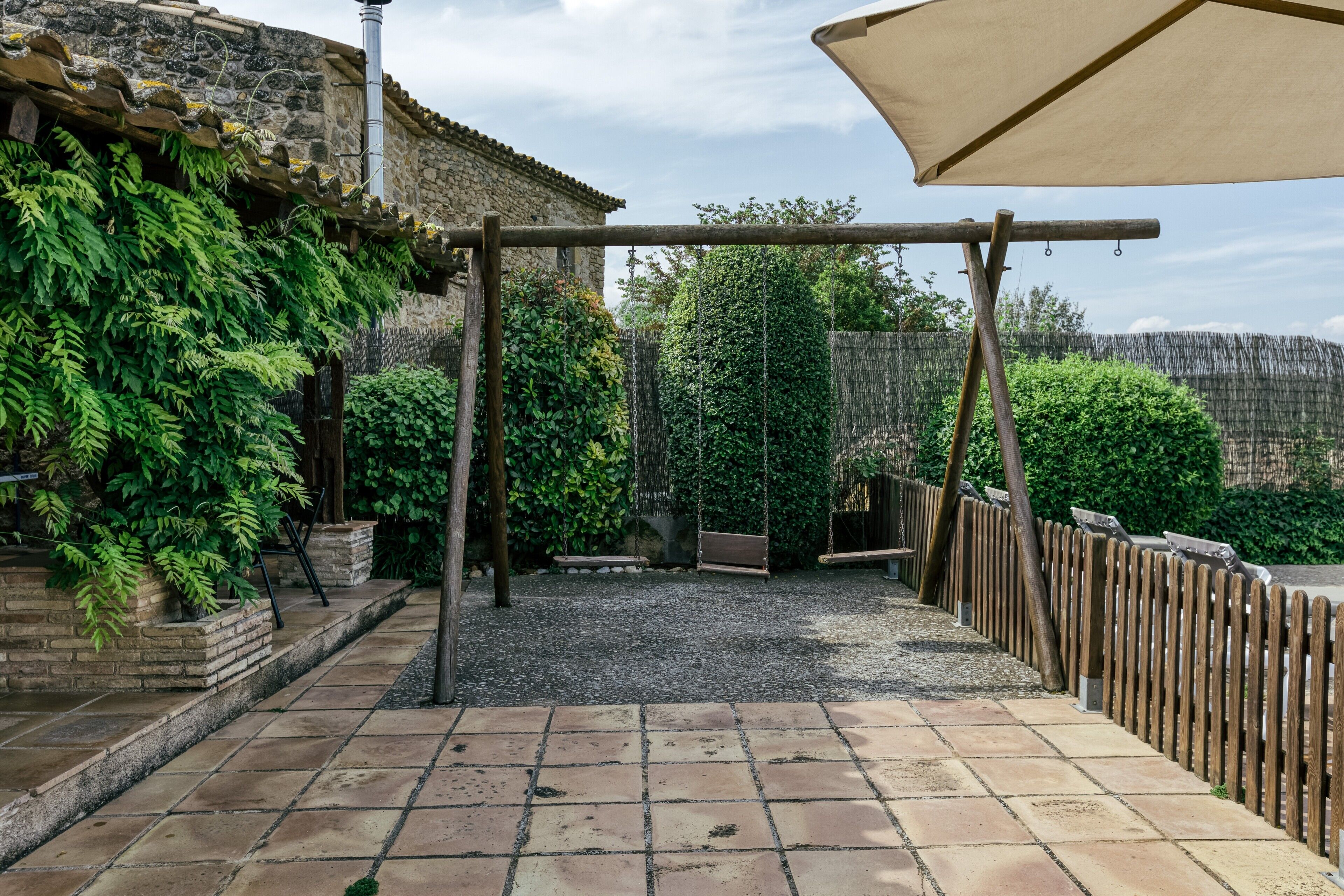 A patio area with a swing set, a pergola, and a wooden fence.