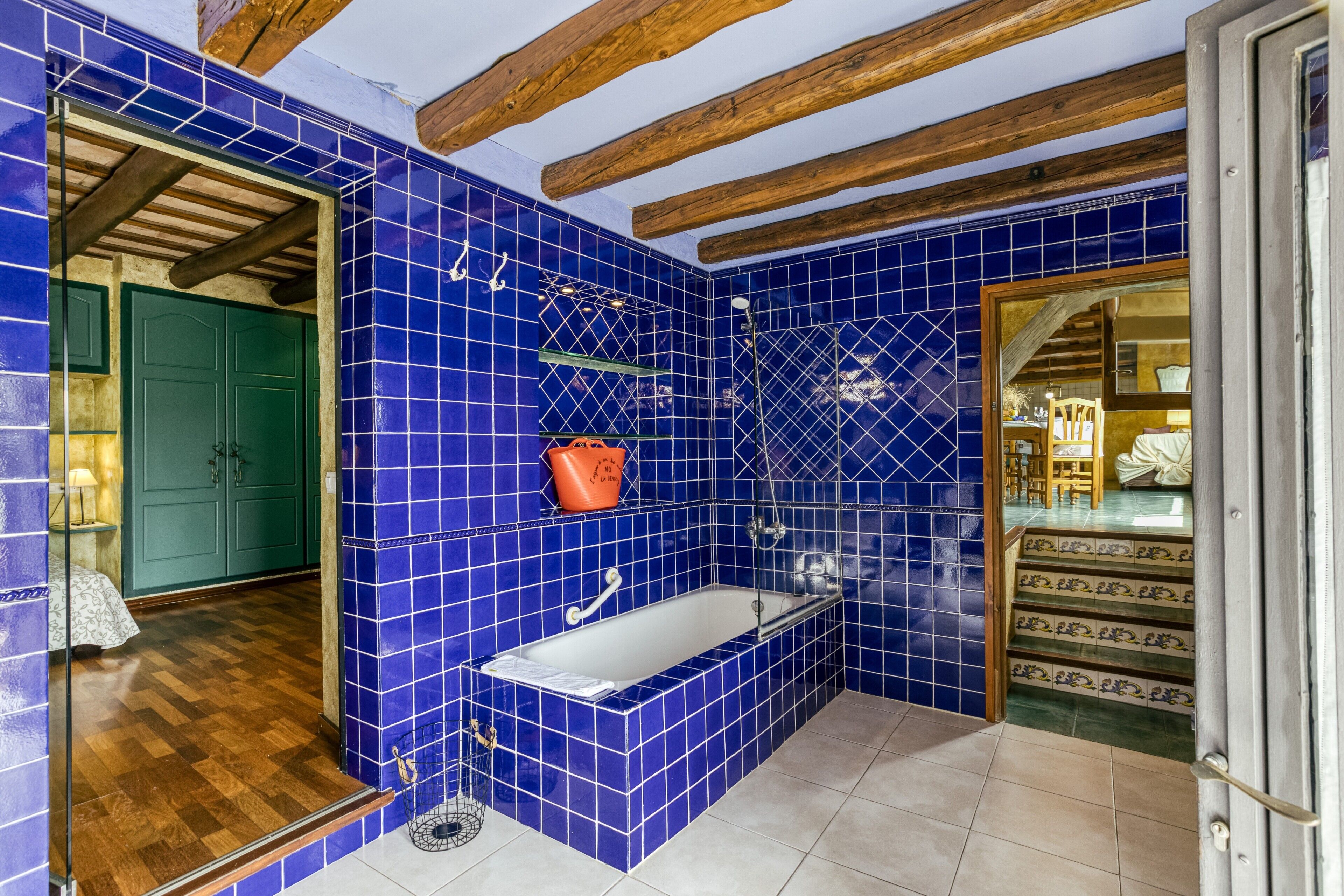 Un baño con azulejos azules, una bañera, ducha y vigas de madera en el techo.