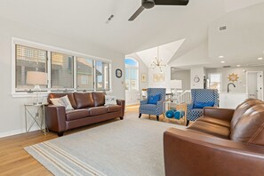 Un salón amplio con un sofá de cuero marrón, sillones con estampado azul y un gran ventanal con persianas.