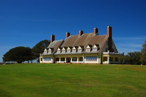 A large, two-story house with a steeply pitched roof, multiple chimneys, and a well-maintained lawn in front.
