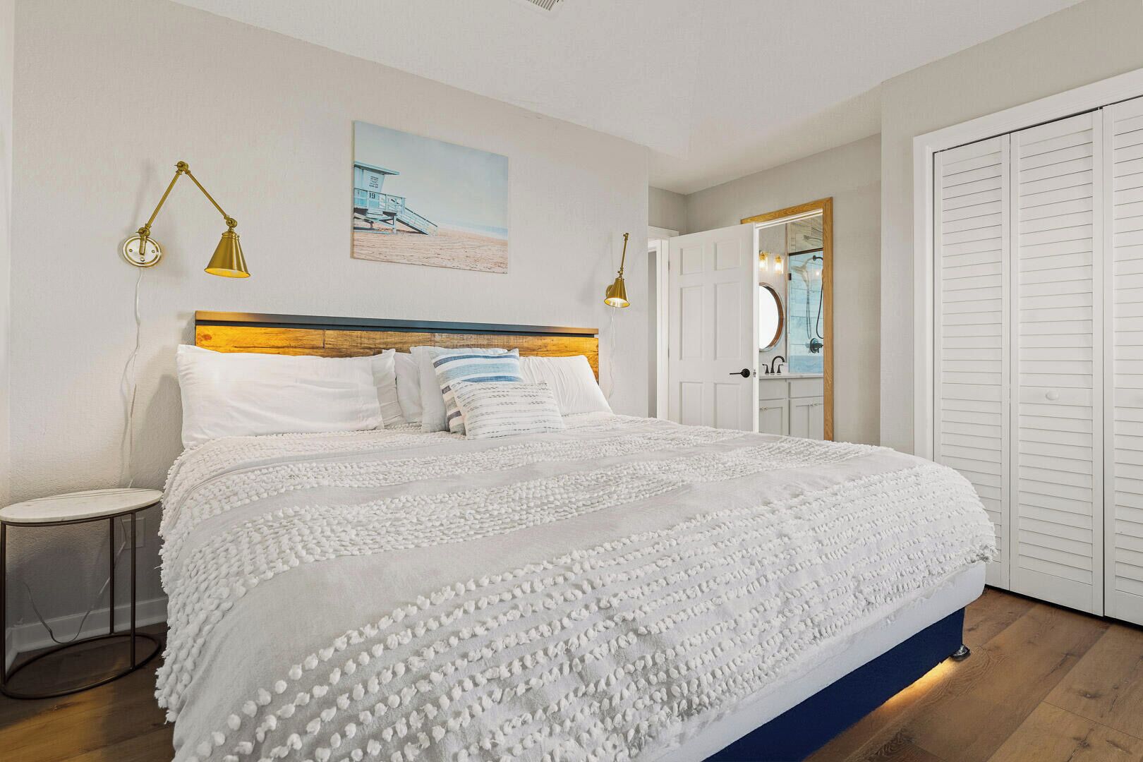 A neatly arranged bedroom with a large bed, a bedside table, a wall-mounted lamp, and a door with a mirror.
