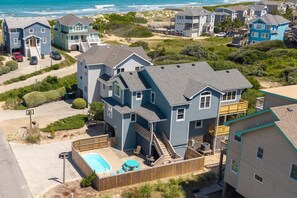 A residential area with multiple houses, a swimming pool, and a beach in the background. - Steps to the Beach 4 Bedroom Home at Crown Point (Corolla)