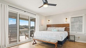 Un dormitorio con una cama grande, un ventilador de techo y vistas a una terraza exterior por una puerta corrediza de vidrio.