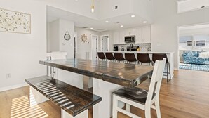 Una cocina moderna con armarios blancos, una isla central y un comedor con una mesa grande y sillas.