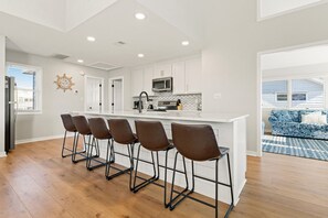 Una cocina moderna con armarios blancos, una isla central con taburetes de bar, un microondas y una estufa.
