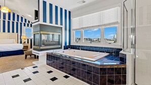 A modern bathroom with a large bathtub, a window with a city view, and striped walls. - Sandbox 8 Bedroom Home in Kitty Hawk Shores (Kill Devil Hills)