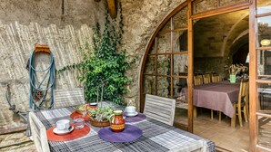 A rustic dining area with a table set for two, a thatched roof, and a stone wall. - Country House 'Cal Secretari' with Shared Pool, Private Terrace and Wi-Fi (SAUS CAMALLERA LLAMPAIES)