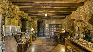 A rustic interior with stone walls, wooden beams, a tiled floor, a reception desk, and various framed items. - Country House 'Cal Secretari' with Shared Pool, Private Terrace and Wi-Fi (SAUS CAMALLERA LLAMPAIES)
