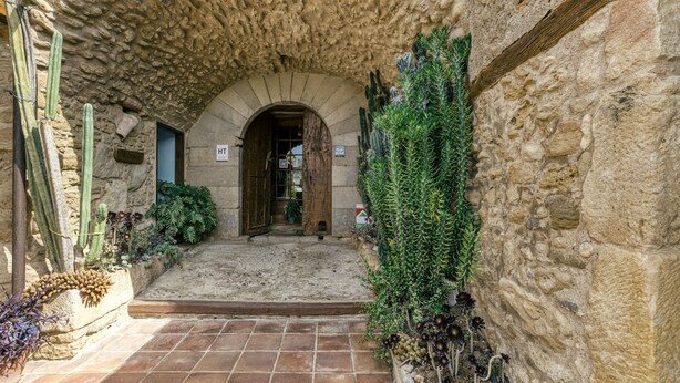 A stone archway leading to a courtyard with cacti and plants, a tiled floor, and a rustic stone wall. - Country House 'Cal Secretari' with Shared Pool, Private Terrace and Wi-Fi (SAUS CAMALLERA LLAMPAIES)