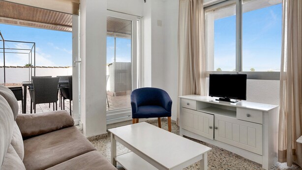 Ein modernes Wohnzimmer mit einer Couch, einem Couchtisch, einem Fernseher auf einer Anrichte und einem Balkon mit Gartenmöbeln.