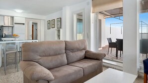 Ein modernes Wohnzimmer mit einer Couch, einem Esstisch und Stühlen. Es gibt eine Küchenzeile mit einem Kühlschrank und einem weiteren Esstisch mit Stühlen.