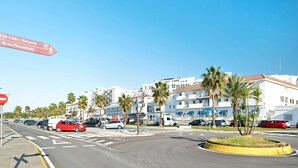 Eine Straße mit Autos, Palmen und einem Hotel mit Balkonen.