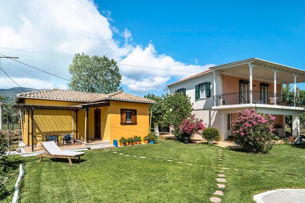 A two-story house with a covered patio, a lawn, and potted plants.