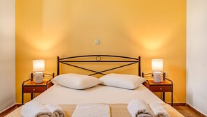 A neatly made bed with two pillows, a bedside table with a lamp, and a wall-mounted light fixture. - Holiday Home 'Garden House Lefkada' with Shared Terrace, Wi-Fi and Air Conditioning (Lefkada)