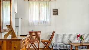 A room with a wooden desk, two wooden chairs, a sofa, a small table, and a window with curtains. - Holiday Home 'Garden House Lefkada' with Shared Terrace, Wi-Fi and Air Conditioning (Lefkada)