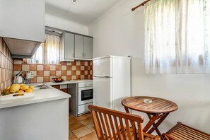 A compact kitchen with a sink, stove, and refrigerator, a wooden table, and a chair.