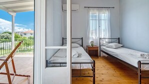 Een kamer met twee eenpersoonsbedden, een houten vloer, een raam met gordijnen, een klein tafeltje met een lamp en een airconditioning.