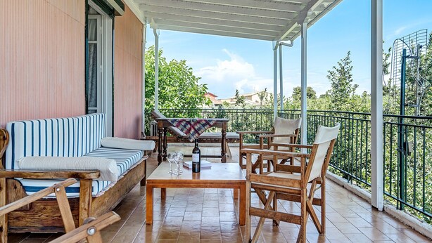 Een overdekt terras met een bank, stoelen en een tafel, met uitzicht op een tuin.