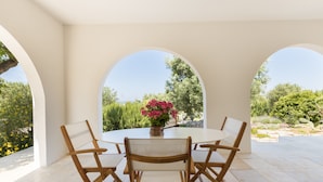 A round table with four chairs, a vase with flowers, and a view of greenery through arches. - "Villa Filara" with Private Pool, Private Terraces & Wi-Fi (carovigno)