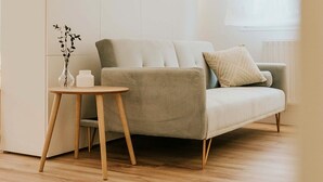 Una sala de estar moderna con un sofá, una pequeña mesa de madera y un florero con ramas.