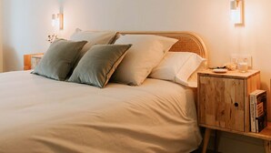 Una cama bien hecha con un cabecero de madera, dos mesitas de noche con lámparas y un aparador con libros.