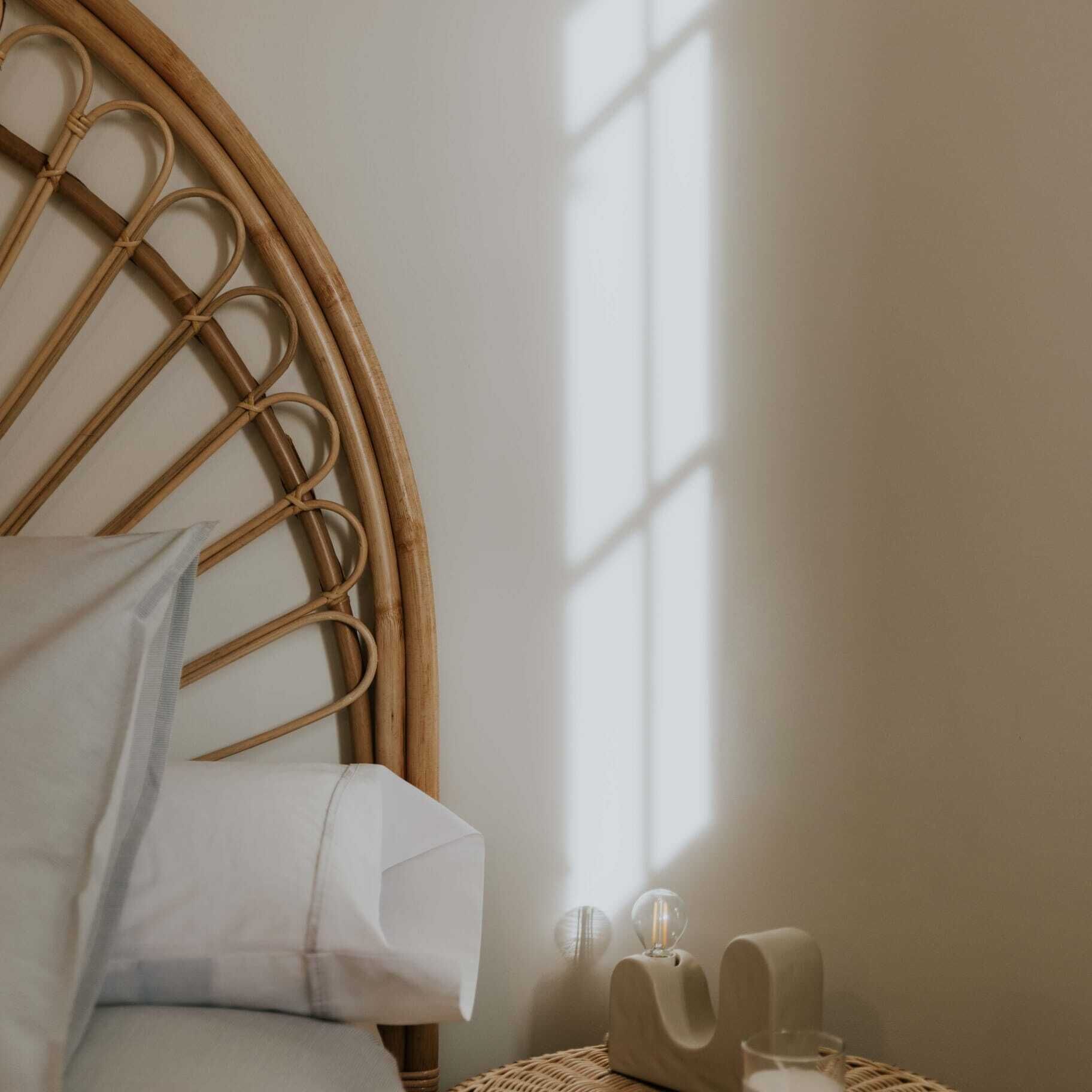 A room with a round wooden bed frame, a white pillow, and a bedside table with a lamp and a glass.