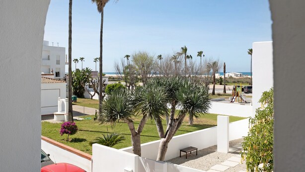 A balcony with a view of palm trees, a playground, and a building in the background.