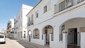 A row of white buildings with balconies, a clear sky, and a street with a parked car.