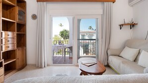 A room with a wooden cabinet, a sofa, a table, and a balcony with a view of buildings and trees.