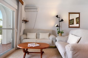 Un salon comprenant un canapé, une table basse, un climatiseur, une lampe et un tableau encadré accroché au mur.