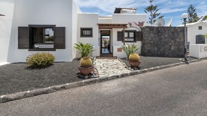 Una casa moderna con un muro in pietra, piante in vaso e cielo sereno.