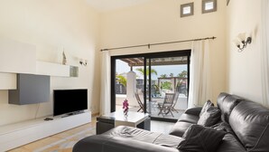 Un soggiorno moderno con una TV a schermo piatto, un divano in pelle, un tavolino da caffè e vista su un patio esterno attraverso una porta scorrevole in vetro.