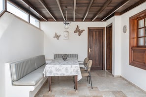A room with a bench, a table with a patterned tablecloth, a chandelier, decorative butterfly wall art, and wooden doors.