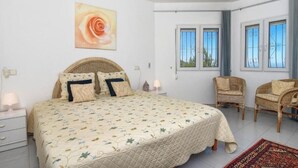 Ein Schlafzimmer mit einem Bett, zwei Stühlen, einem Fenster und einem Deckenventilator.
