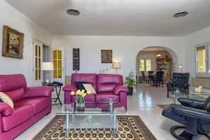 A spacious living room with a large sofa, a coffee table, and a dining area in the background.