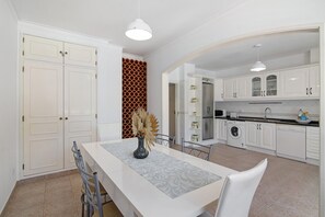 A modern kitchen with white cabinets, a dining table with chairs, and a hanging light fixture.