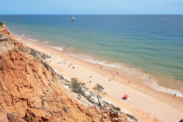 A beach with a cliff, clear sky, and calm sea.