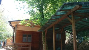 A wooden cabin with a covered porch, a window with curtains, and a wooden fence.
