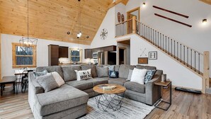 A spacious living area with a large sectional sofa, a wooden ceiling, and a staircase leading to an upper level.