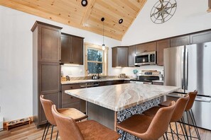 Una cocina moderna con armarios de madera, electrodomésticos de acero inoxidable, una isla de mármol y taburetes de cuero.